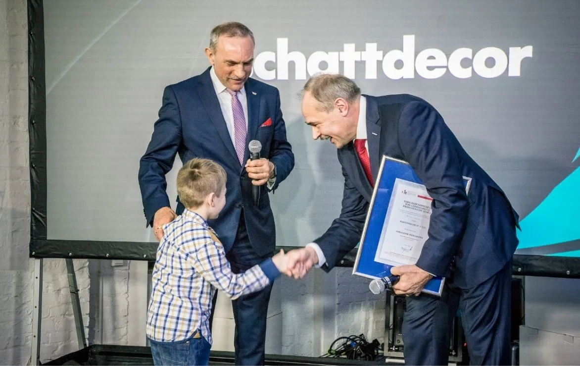 Jan Szynaka i prezes Schattdecor stoją na scenie z wnukiem Jana Szynaki podczas jubileuszu firmy