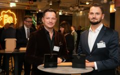 Dwaj mężczyźni w eleganckich marynarkach stoją przy okrągłym stoliku podczas gali meblarskiej. Przed nimi na blacie leżą dwie czarne statuetki „Diament Meblarstwa 2026”. W tle widoczne są inne osoby oraz neonowy logotyp.