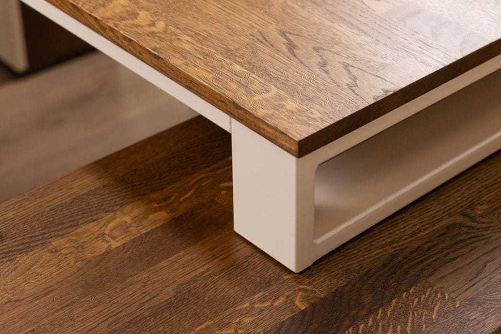 Zbliżenie na detal konstrukcyjny mebla marki Deerhorn. Połączenie grubego blatu z naturalnego drewna dębowego o wyraźnym usłojeniu z białą, metalową nogą o profilu prostokątnym.