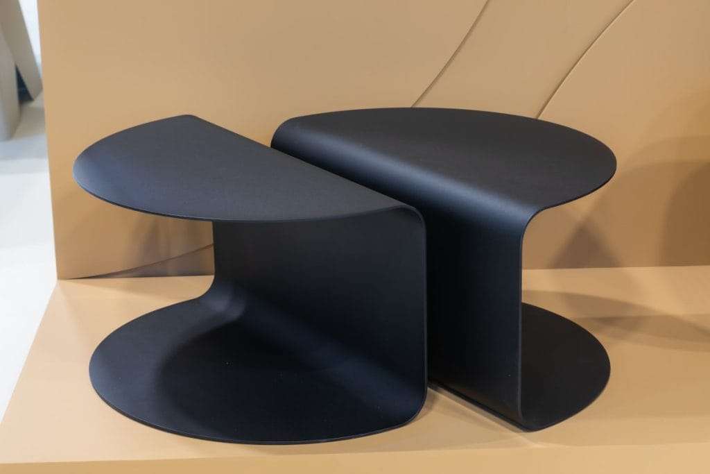 Nowoczesny, czarny stolik kawowy Paco o minimalistycznym, geometrycznym kształcie litery C, wykonany z giętego metalu, zaprezentowany na beżowym tle ekspozycji.