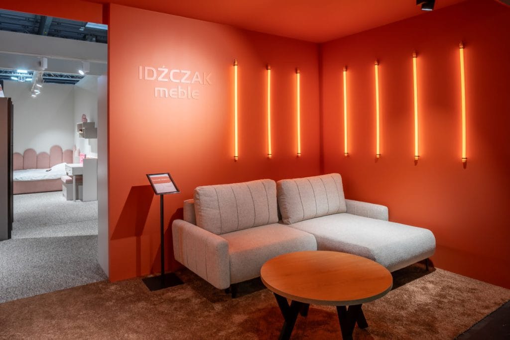 Idźczak Meble na targach Meble Polska 2025 w Poznaniu - bialy narożnik na pomarańczowej ścianie
