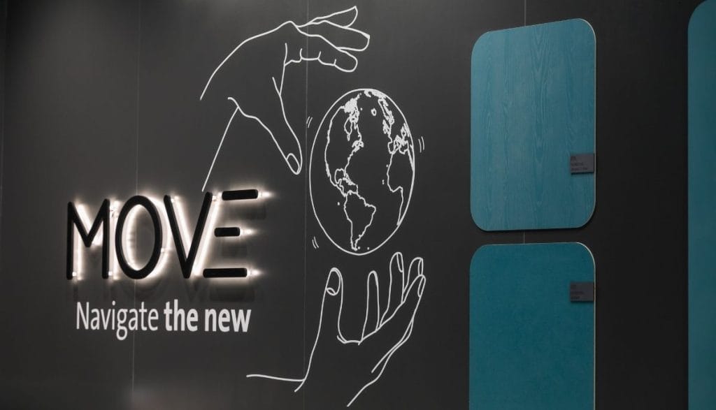 Ściana ekspozycyjna Impress Decor z podświetlanym napisem MOVE i grafiką globu. Obok widoczne pionowe panele dekoracyjne w odcieniach morskich. Detal prezentujący nowoczesny branding firmy stawiającej na globalne trendy i innowacyjne materiały meblowe.