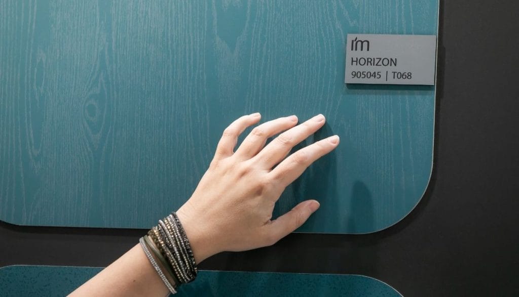 Zbliżenie na dłoń dotykającą powierzchni panelu meblowego w kolorze Petrol Horizon (905045) od Impress Decor. Zdjęcie akcentuje haptyczne właściwości dekoru i jego unikalną strukturę, co jest istotnym argumentem w rozmowach biznesowych z producentami mebli.
