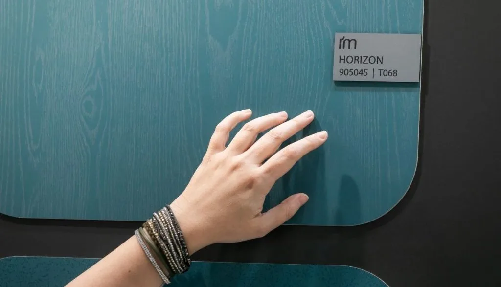 Zbliżenie na dłoń dotykającą powierzchni panelu meblowego w kolorze Petrol Horizon (905045) od Impress Decor. Zdjęcie akcentuje haptyczne właściwości dekoru i jego unikalną strukturę, co jest istotnym argumentem w rozmowach biznesowych z producentami mebli.