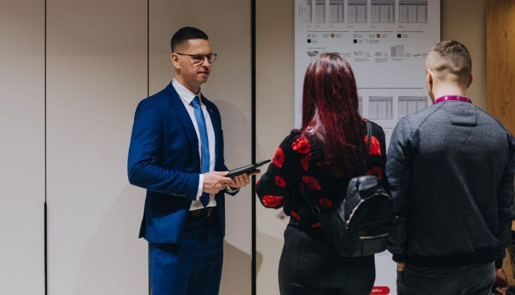 Doradca w niebieskim garniturze prezentuje ofertę produktową na stoisku Meble Polska 2026 w ramach obchodów jubileuszu Meble Wójcik 40 lat.