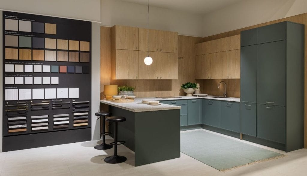 Ekspozycja nowoczesnej szałwiowej kuchni z wyspą i tablicą wzorników materiałów na stoisku Meble Polska 2026, przygotowana na Meble Wójcik 40 lat.