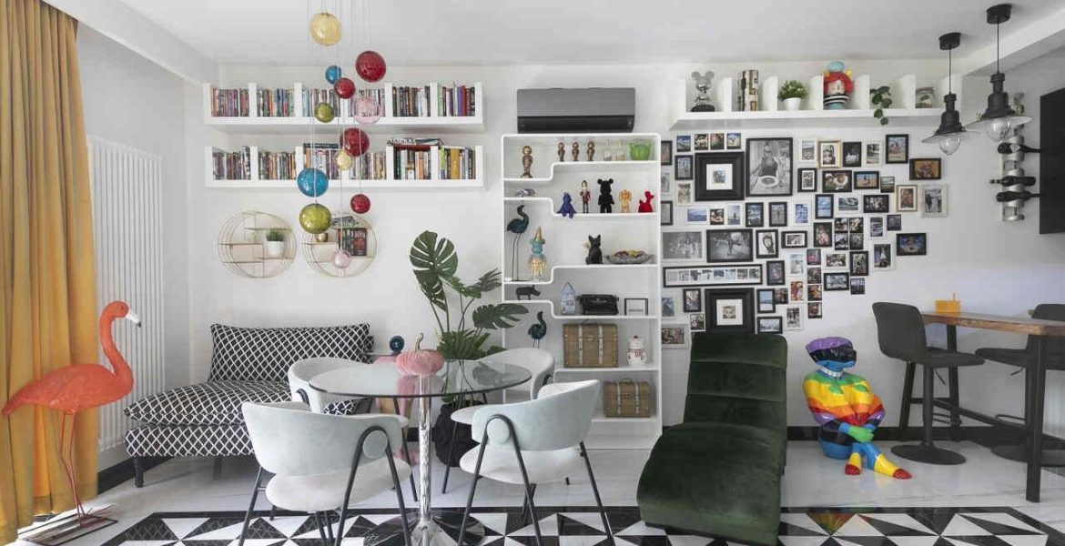 Ten eklektyczny salon łączy różnorodne style i tekstury, tworząc dynamiczną przestrzeń. Wzrok przyciąga biało-czarna podłoga, która kontrastuje z intensywnymi kolorami mebli. Ściany zdobią liczne zdjęcia mieszkańców, nadające wnętrzu osobisty charakter. Całość pobudza zmysły i inspiruje do twórczego działania.