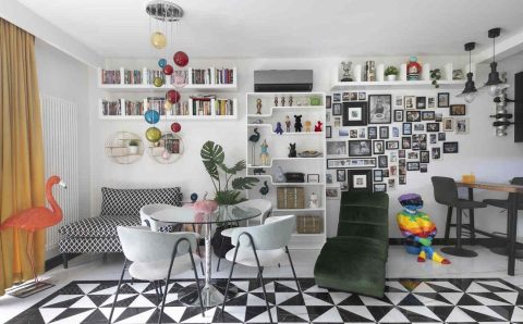 Ten eklektyczny salon łączy różnorodne style i tekstury, tworząc dynamiczną przestrzeń. Wzrok przyciąga biało-czarna podłoga, która kontrastuje z intensywnymi kolorami mebli. Ściany zdobią liczne zdjęcia mieszkańców, nadające wnętrzu osobisty charakter. Całość pobudza zmysły i inspiruje do twórczego działania.