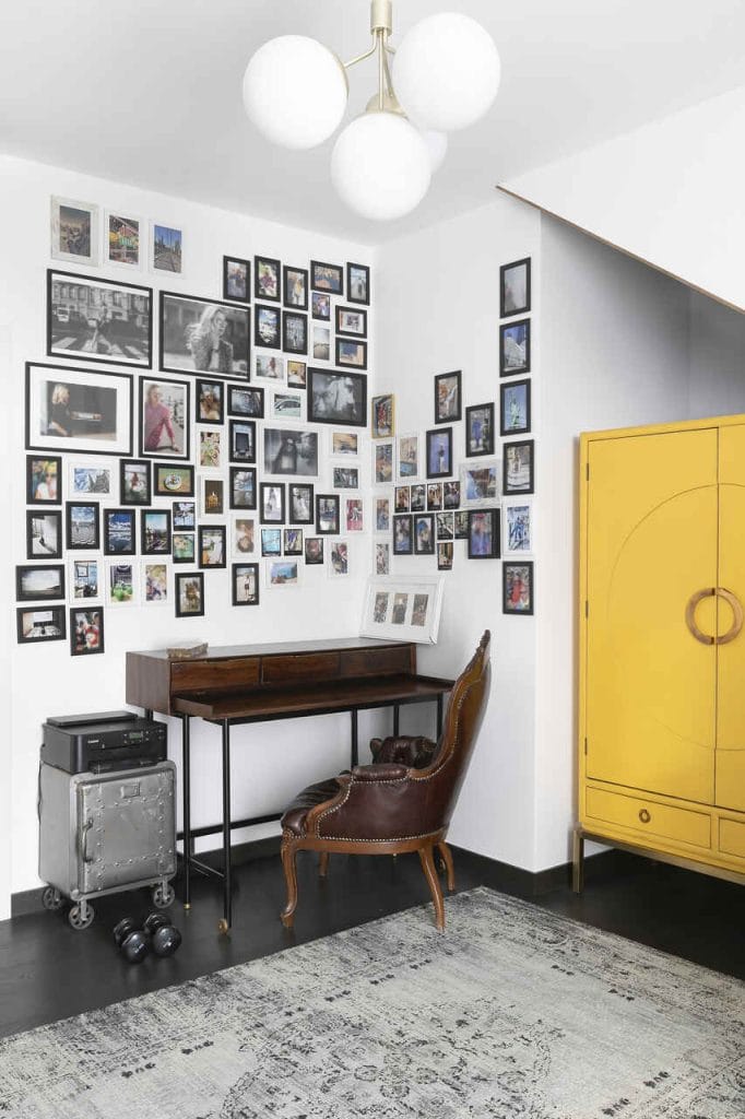 Stare, ciemne biurko w antycznym stylu to prawdziwa perełka właścicielki. Ciężki fotel dodaje klasycznej wagi i elegancji. Na ścianie galeria zdjęć, nadająca przestrzeni osobisty charakter. Obok, żółta szafa na smukłych nóżkach wprowadza lekkość, subtelnie kontrastując z bardziej masywnymi elementami wnętrza.