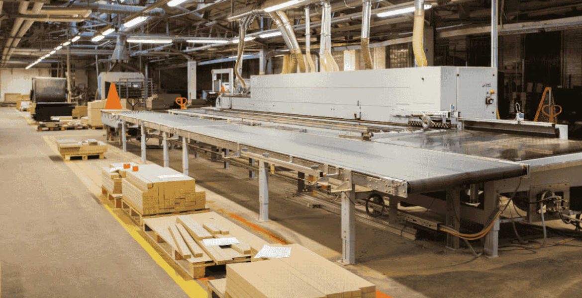 Park maszynowy w nowoczesnym zakładzie obróbki drewna. Widoczna linia produkcyjna do prefabrykacji mebli oraz przygotowane komponenty drewniane na paletach wzdłuż ciągu komunikacyjnego.