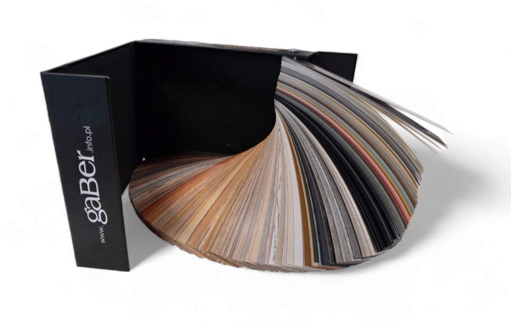 Otwarty, profesjonalny wzornik obrzeży meblowych marki gaBer w eleganckim, czarnym etui z logo i adresem strony www. Wzornik jest rozłożony w wachlarz, prezentując setki próbek kolorów i tekstur: od szerokiej gamy dekorów drewnopodobnych, przez kolory jednolite (uni), aż po imitacje kamienia i betonu. Niezbędne narzędzie dla projektantów wnętrz i stolarzy.