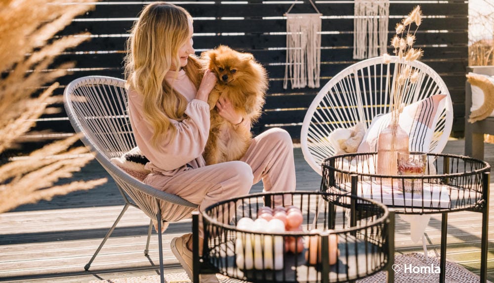 Kobieta z małym psem na kolanach siedzi na meblach ogrodowych z rattanu