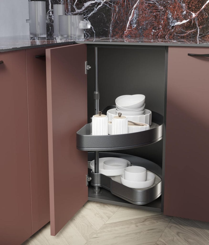 Nowoczesna szafka narożna z systemem obrotowych półek (karuzela) w kuchni z bordowymi frontami. Na wysuniętej półce znajduje się biała zastawa stołowa i ozdobne słoiki z drewnianymi pokrywkami.