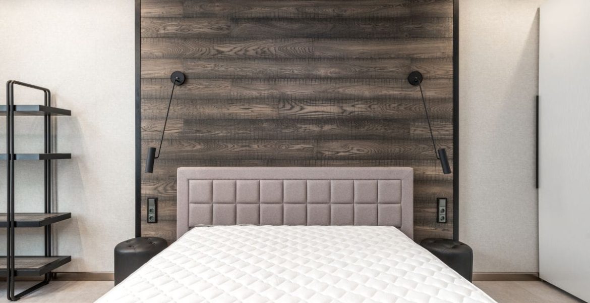 Łóżko widziane en face, tapicerowany zagłówek, drewniana ściana.