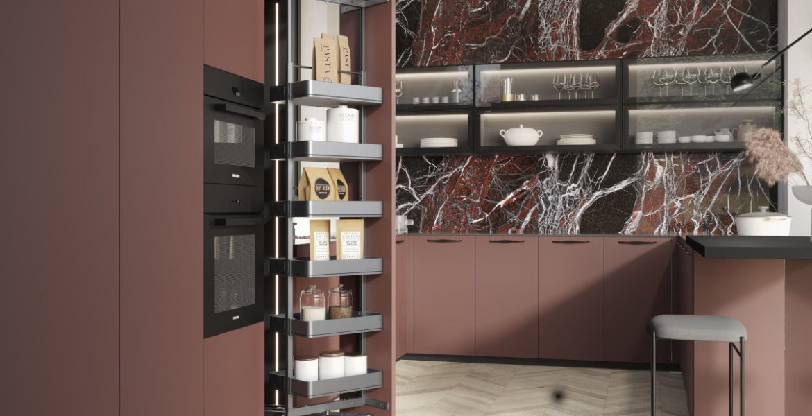 Otwarta wysoka szafka cargo w nowoczesnej kuchni z frontami w odcieniu rdzawej czerwieni i blatem z ciemnego marmuru. Wielopoziomowy system wysuwny z koszami wypełnionymi zapasami jedzenia, słoikami, torebkami makaronu i puszkami.