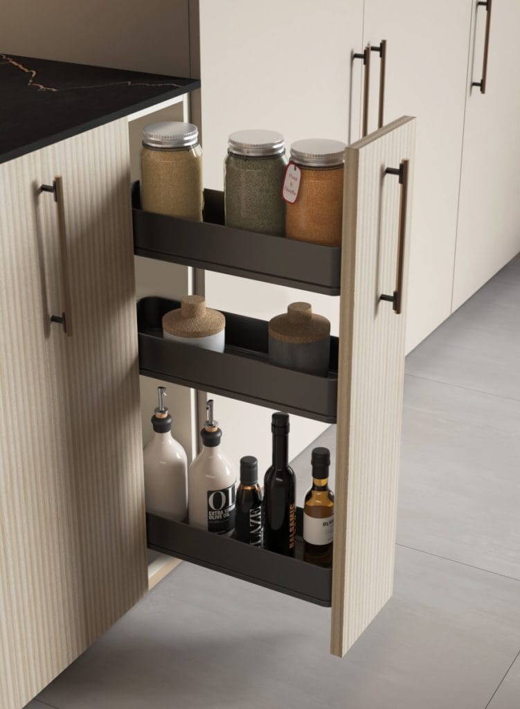 Wąska szafka wysuwna typu cargo w dolnej zabudowie kuchennej z frontami z jasnego drewna. Trzy poziomy metalowych koszy wypełnione słoikami z przyprawami, oliwą i octem.