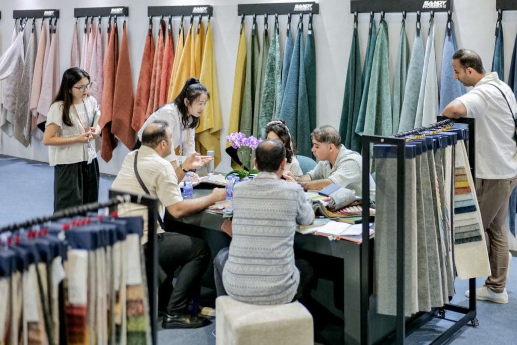 Intertextile Shanghai Home Textiles - ludzie na stoisku na targach oglądający tkaniny