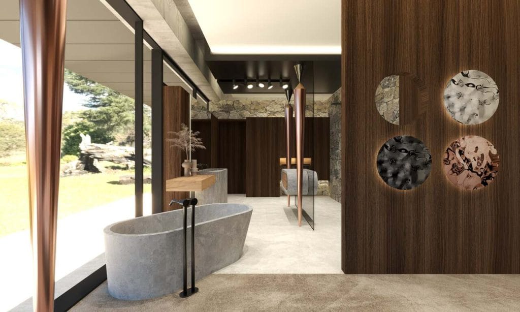 Salon łazienkowy otwarty na główną sypialnię. Na granicy tych stref znalazła miejsce odlana z betonu wolno stojąca wanna. Podobne betonowe formy tworzą umywalkę i półkę zawieszoną na szklanej ścianie oddzielającej przestrzeń podwójnego prysznica. Po obu stronach kamiennej ściany znajduje się przejście do ukrytej za nią strefy WC. Elementem przewodnim połączonej przestrzeni sypialni, łazienki i garderoby są miedziane kolumny uformowane na kształt ostrych stożków. Wnętrze pochodzi z podkrakowskiej rezydencji o powierzchni ok. 1,4 tys. m2. Projekt: Michał Swałtek/Kaja Swałtek, Swałtek Design Studio.