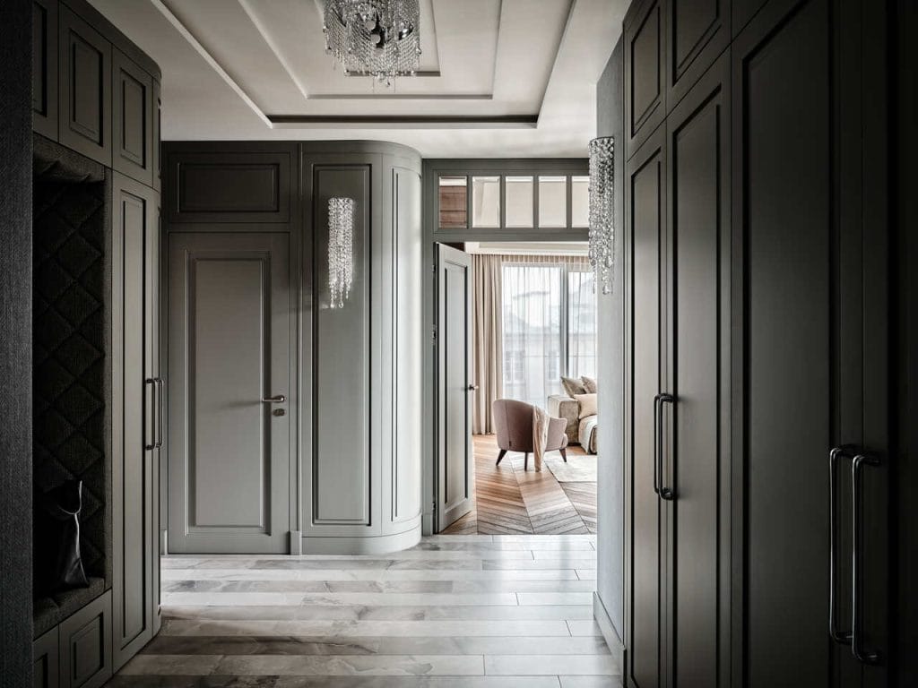 Wnętrze to ciekawe połączenie klasycyzującej architektury z elementami klasyki w nowoczesnym budynku wkomponowanym w zabytkowy kwartał Warszawy. Połączenie kamiennej podłogi w paski (dwa kolory marmuru) z projektowanymi zabudowami; zaoblenie ściany łazienki, a także poszerzenie otworu prowadzącego do salonu – pozwoliły na połączenie holu z salonem. Umożliwiło także przelewanie się przestrzeni i jednoczesne doświetlenie holu naturalnym światłem. Projekt: arch. Roland Stańczyk, RS Studio Projektowe. Fot. Piotr Gęsicki.