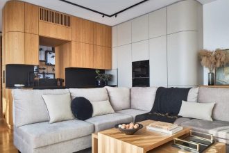 Jednoprzestrzenna kuchnia połączona z salonem. Naturalny dąb połączony z czarnym granitem, który dobrze sprawdza się na blatach. W kuchni jest otwór w zabudowie, łączący kuchnię z klatką schodową. Otwór powstał w wyniku zabudowy obłym elementem meblowym słupa (taka była konstrukcja budynku). Projektant zostawił otwór, aby osoba pracująca w kuchni miała komunikację z przestrzenią klatki schodowej, gdzie się otwiera widok na dwie kondygnacje. Projekt: arch. Roland Stańczyk, RS Studio Projektowe. Fot. Budzik Studio.