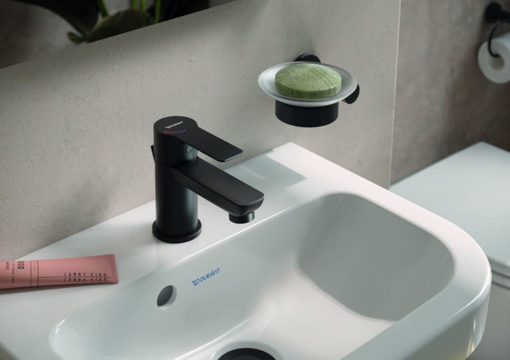 Umywalka D-Code to kompaktowe rozwiązanie do toalet gościnnych – oferuje pojemną misę i praktyczne blaty boczne. Czarne baterie i akcesoria dodają wyrazistości i nowoczesnego stylu.