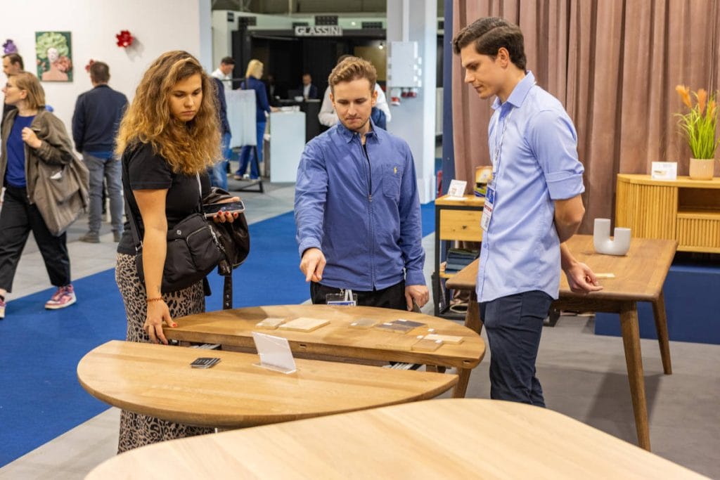 Warsaw Home & Contract - troje ludzi na stoisku na targach oglądający stół