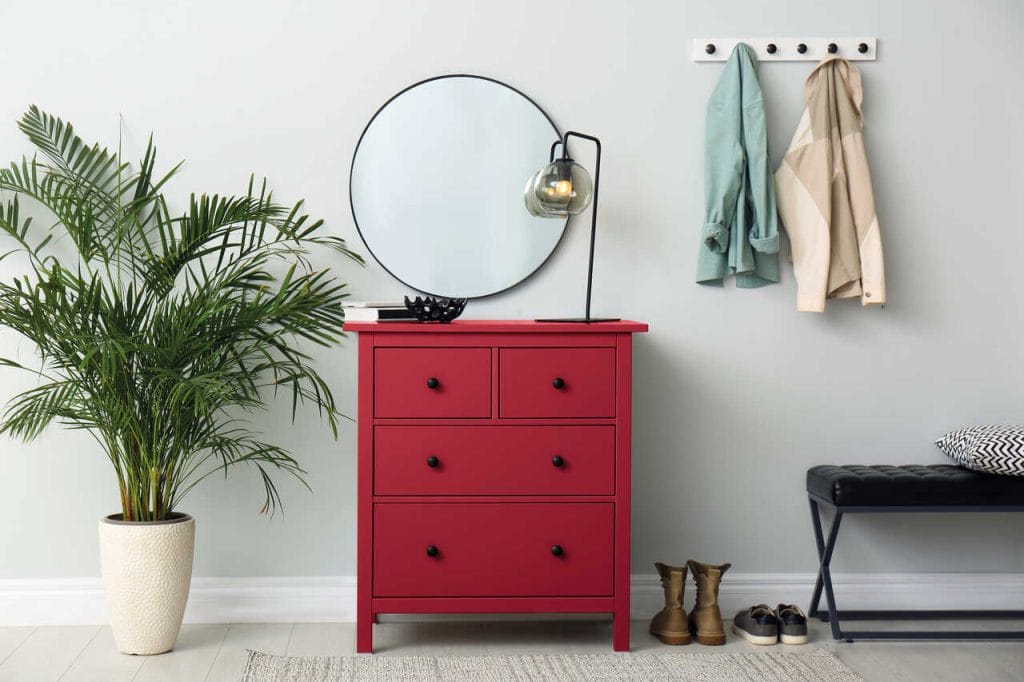 Wykorzystanie śmiałej czerwieni to pomysł na metamorfozę przedpokoju w niewyróżniającym klasycznym stylu. Na tle delikatnej szarości komoda w odcieniu Red Deluxe z palety Beckers Designer Universal wysunie się na pierwszy plan. Łatwy do samodzielnego przeprowadzenia zabieg przemalowania dość przeciętnej komody jest więc sposobem na przełamanie konwencjonalnego wyglądu strefy wejściowej. Dodatkową dynamikę do tej typowo użytkowej przestrzeni wprowadzi pokaźnych rozmiarów palma doniczkowa.