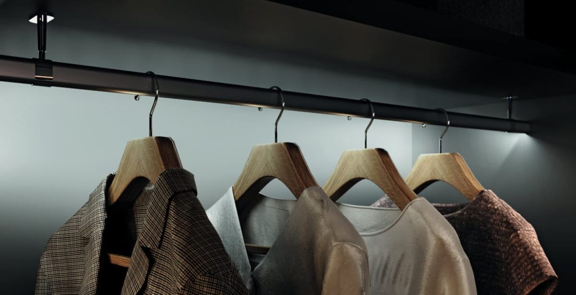 Hafele - Ubrania zawieszone na drewnianych wieszakach w eleganckiej, podświetlonej garderobie