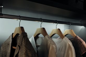 Hafele - Ubrania zawieszone na drewnianych wieszakach w eleganckiej, podświetlonej garderobie