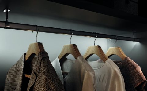 Hafele - Ubrania zawieszone na drewnianych wieszakach w eleganckiej, podświetlonej garderobie