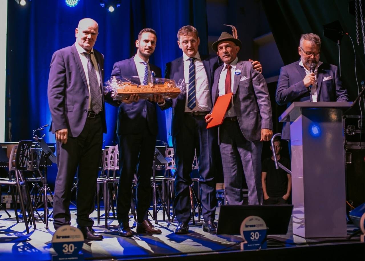 Jan Szynaka stoi na scenie z czterema przedstawicielami Kronospan podczas branżowej imprezy