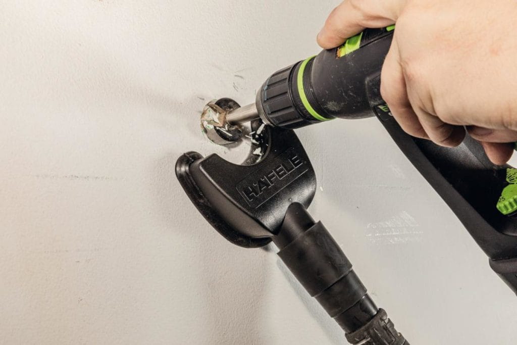 Osoba wierci otwór w ścianie za pomocą wiertarki, korzystając z przystawki odsysającej pył marki Häfele.