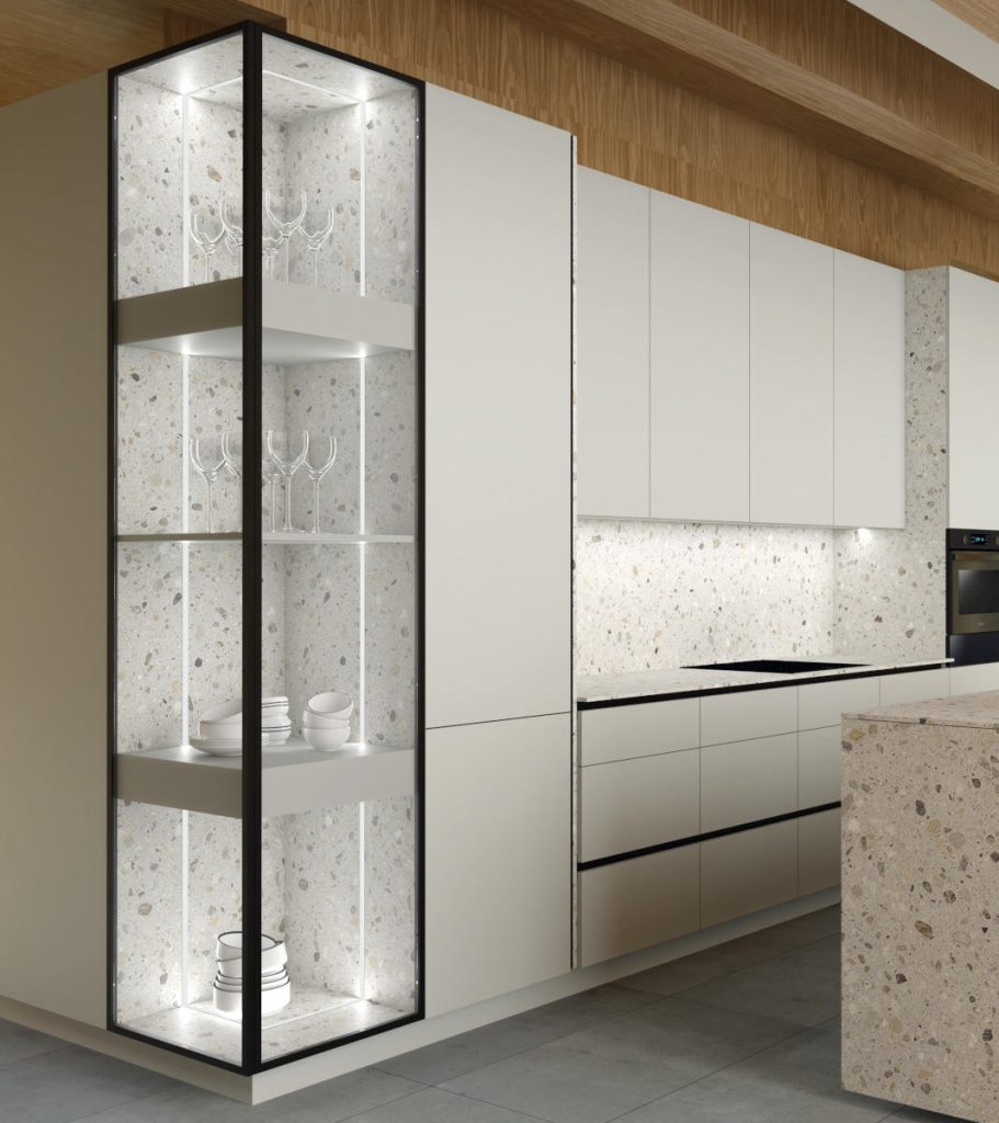 Nowoczesna kuchnia z pionową przeszkloną witryną LED, czarnymi profilami i półkami z oświetleniem, w zabudowie z jasnymi frontami i kamiennym wykończeniem.