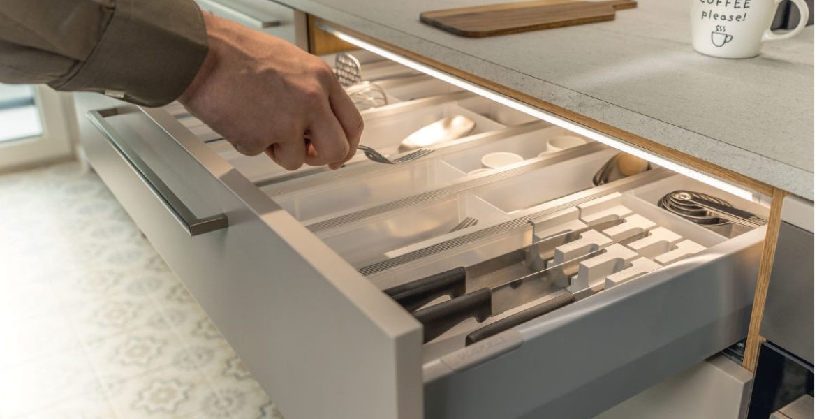 Detal otwartej szuflady kuchennej z wkładem na sztućce, oświetlonej od góry dyskretną listwą LED Loox5. Światło precyzyjnie doświetla zawartość szuflady, ułatwiając znalezienie przyborów kuchennych.