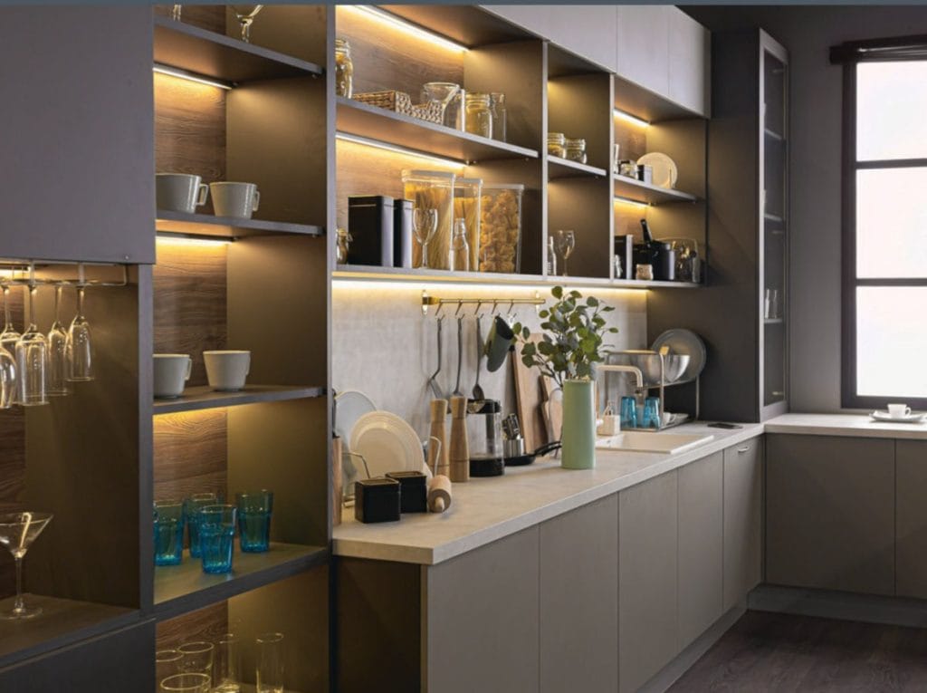 Nowoczesna kuchnia z rozbudowanym systemem oświetlenia meblowego. Ciepłe światło LED zamontowane pod półkami oraz wewnątrz witryn eksponuje naczynia i akcesoria kuchenne, tworząc przytulną atmosferę i doświetlając blat roboczy.