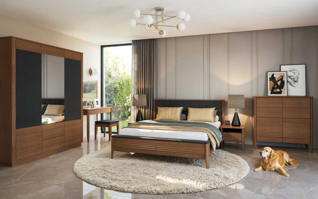 Sypialnia z kolekcji TANGO firmy Mebin w wybarwieniu dąb rustic, oparta na naturalnych surowcach i wyważonych proporcjach, wyróżnia się ciepłym, szlachetnym charakterem. Paleta beży, brązów i tonów taupe sprzyja wyciszeniu i buduje atmosferę sprzyjającą regeneracji. Pionowe podziały ścian porządkują kompozycję, natomiast połyskująca posadzka tworzy subtelny kontrast z miękką strukturą dywanu wyznaczającego miejsce wypoczynku. Centralnie zlokalizowane, solidne łóżko z drewnianą ramą i tapicerowanym zagłówkiem, staje się, wraz z szafkami nocnymi, dominantą wizualną aranżacji. Pojemna szafa odznacza się lustrem powiększającym optycznie przestrzeń i dynamicznym frezowaniem o zróżnicowanej głębokości. Sparowana z lustrem i stołkiem, smukła toaletka ustawiona przy oknie zachwyca precyzyjnie opracowanymi detalami, spójnymi w całej serii. Całość łączy prostotę współczesnego wzornictwa z rzemieślniczą jakością i ponadczasową elegancją.