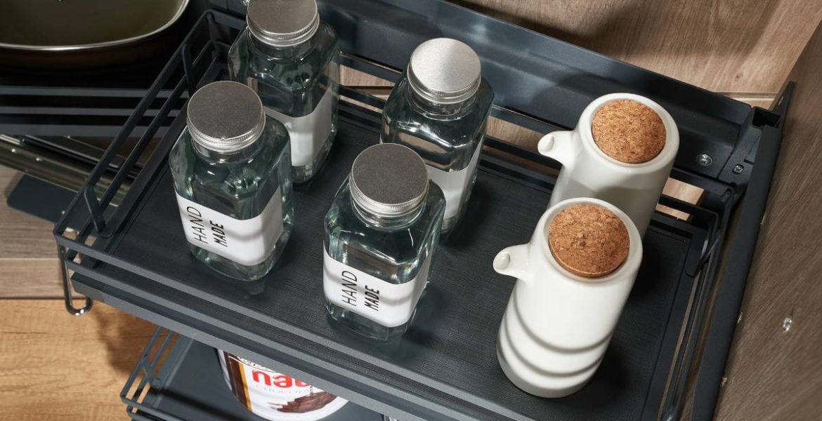 Detal górnej półki cargo AMIX z matą antypoślizgową. Na półce ustawione szklane słoiki i ceramiczne dozowniki na oliwę w nowoczesnej aranżacji kuchennej.