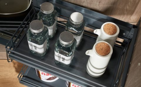 Detal górnej półki cargo AMIX z matą antypoślizgową. Na półce ustawione szklane słoiki i ceramiczne dozowniki na oliwę w nowoczesnej aranżacji kuchennej.