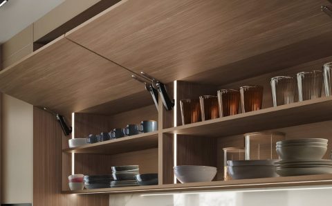 Drewniane szafki kuchenne z systemem bezuchwytowego otwierania Häfele Free Space. Widoczne otwarte fronty typu klapa z dyskretnym mechanizmem podnośnika i podświetleniem LED wnętrza szafek.