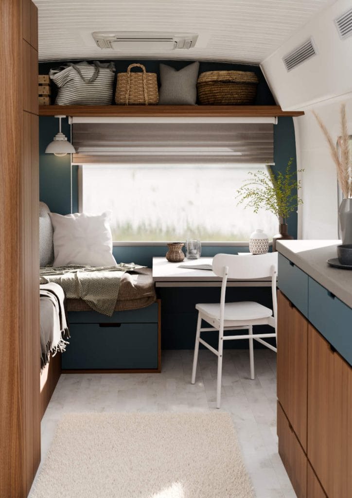 Aranżacja wnętrza kampera typu mobile home z wykorzystaniem dekoru orzechowego Epona Walnut oraz matowych, niebieskich frontów. Funkcjonalna strefa wypoczynkowa z biurkiem i jasną tapicerką w duchu compact living.
