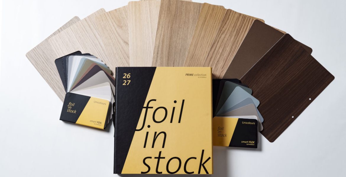 Żółto-czarny katalog Schattdecor „Foil in Stock” na tle rozłożonych próbek folii meblowych w różnych odcieniach drewna i szarości.