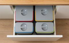 Widok z góry na szufladę kuchenną wypełnioną czterema szczelnie zamkniętymi pojemnikami do segregacji z kolorowymi oznaczeniami.