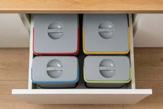 Widok z góry na szufladę kuchenną wypełnioną czterema szczelnie zamkniętymi pojemnikami do segregacji z kolorowymi oznaczeniami.