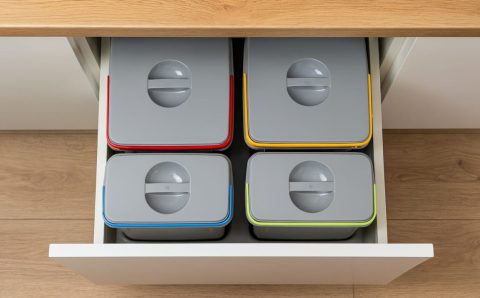 Widok z góry na szufladę kuchenną wypełnioną czterema szczelnie zamkniętymi pojemnikami do segregacji z kolorowymi oznaczeniami.