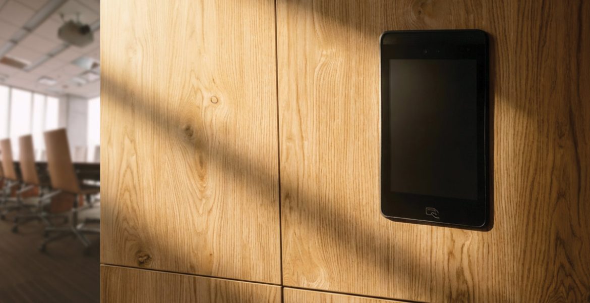 Elektroniczny zamek meblowy z ekranem dotykowym zamontowany w dębowej zabudowie biurowej. Nowoczesne okucia i systemy kontroli dostępu do szafek.