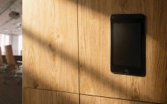 Elektroniczny zamek meblowy z ekranem dotykowym zamontowany w dębowej zabudowie biurowej. Nowoczesne okucia i systemy kontroli dostępu do szafek.