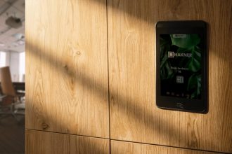 Elektroniczny zamek meblowy z ekranem dotykowym zamontowany w dębowej zabudowie biurowej. Nowoczesne okucia i systemy kontroli dostępu do szafek.