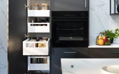 Wnętrze nowoczesnej, ciemnoszarej szafki kuchennej z kilkoma wysuniętymi białymi szufladami. W szufladach widać słoiki z sypkimi produktami, przyprawy, makaron i płatki. Po prawej stronie widać czarny piekarnik do zabudowy. Na blacie obok szafki stoi koszyk z owocami i zioła w doniczkach.