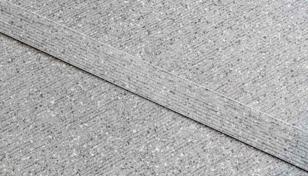 Zbliżenie na szarą powierzchnię o strukturze kamienia, gdzie obrzeża meblowe RAUKANTEX idealnie odwzorowują wzór i fakturę płyty meblowej.