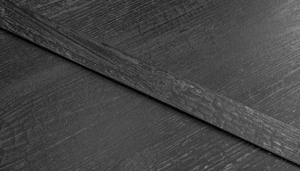 Detale struktury powierzchni płyty oraz dopasowane do niej wzorniczo obrzeża meblowe RAUKANTEX o fakturze ciemnego drewna, prezentujące bezspoinowe połączenie.